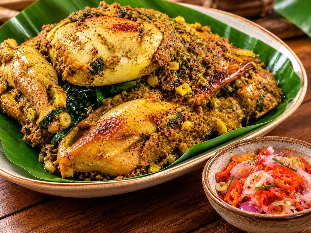 Ayam ungkeb berbumbu rempah di atas daun pisang dengan sambal